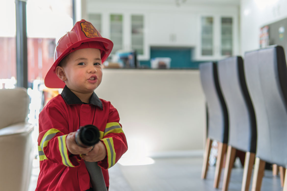 photo of toddler dressed as a fire man holding a hose 